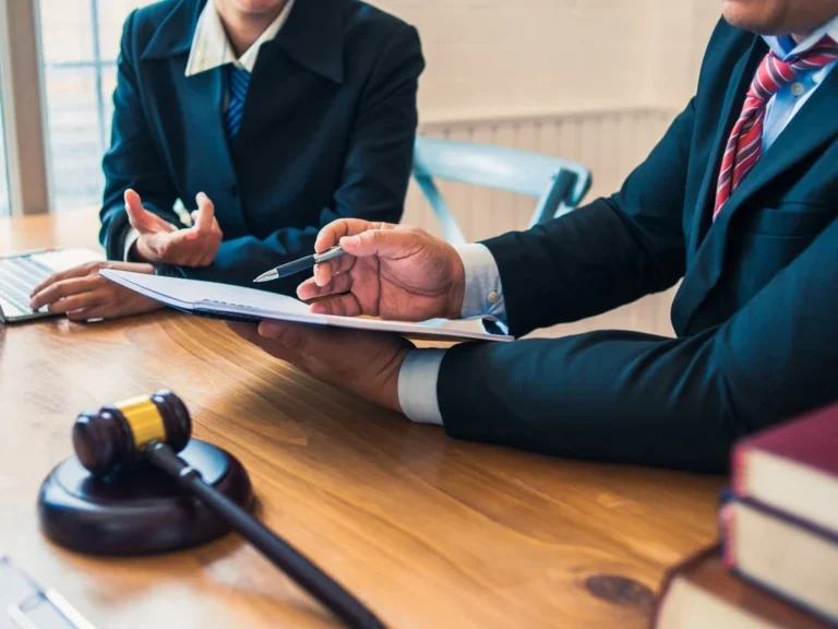 A man and woman in business attire sit together at a desk, engaged in a discussion or meeting.