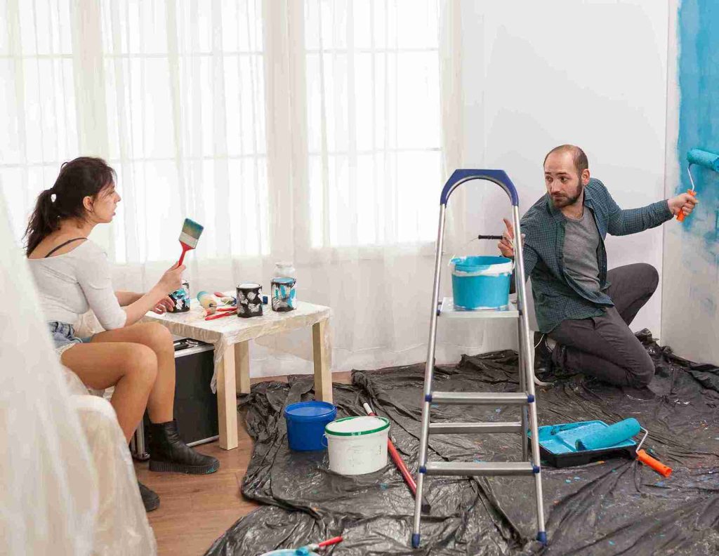 A couple painting a room in bright blue, smiling as they work together to transform their space